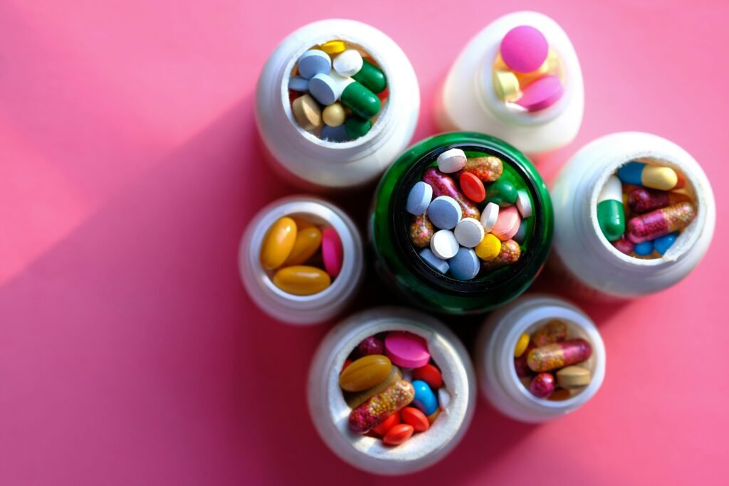 Top view of various medication pills and capsules in containers with bright pink backdrop.