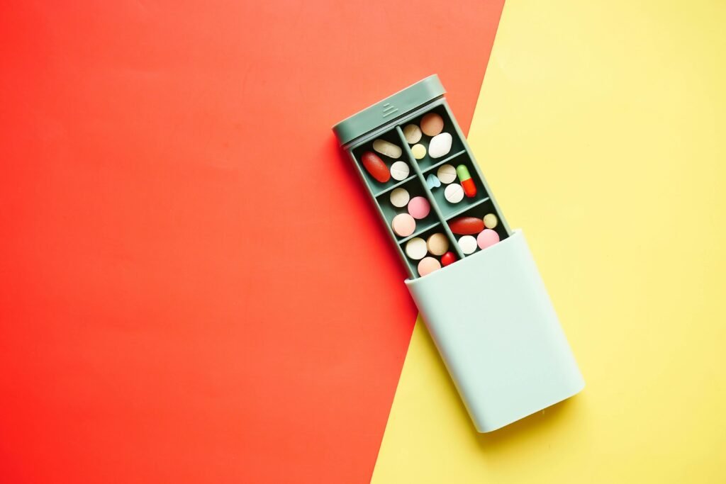 A pill organizer filled with colorful tablets on a bold red and yellow background, emphasizing healthcare.