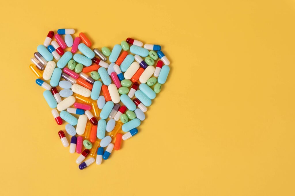 A heart-shaped cluster of multicolored pills on a vibrant yellow background, symbolizing healthcare and medicine.