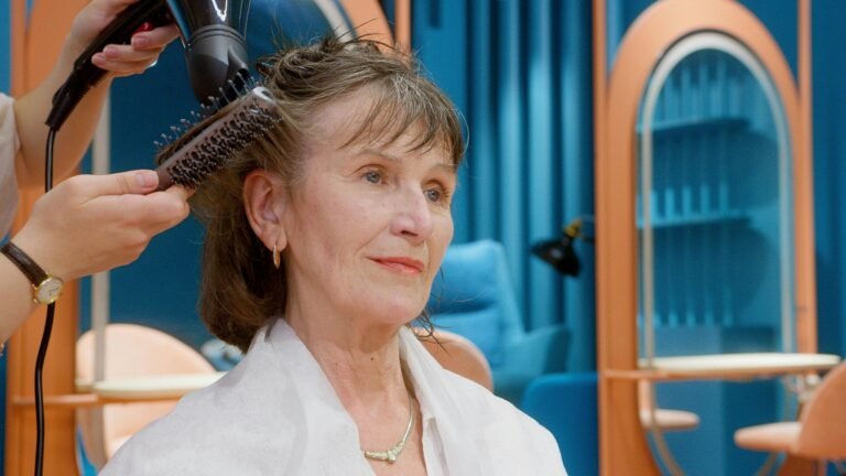 A senior woman receives hairstyling and pampering in a modern salon setting.