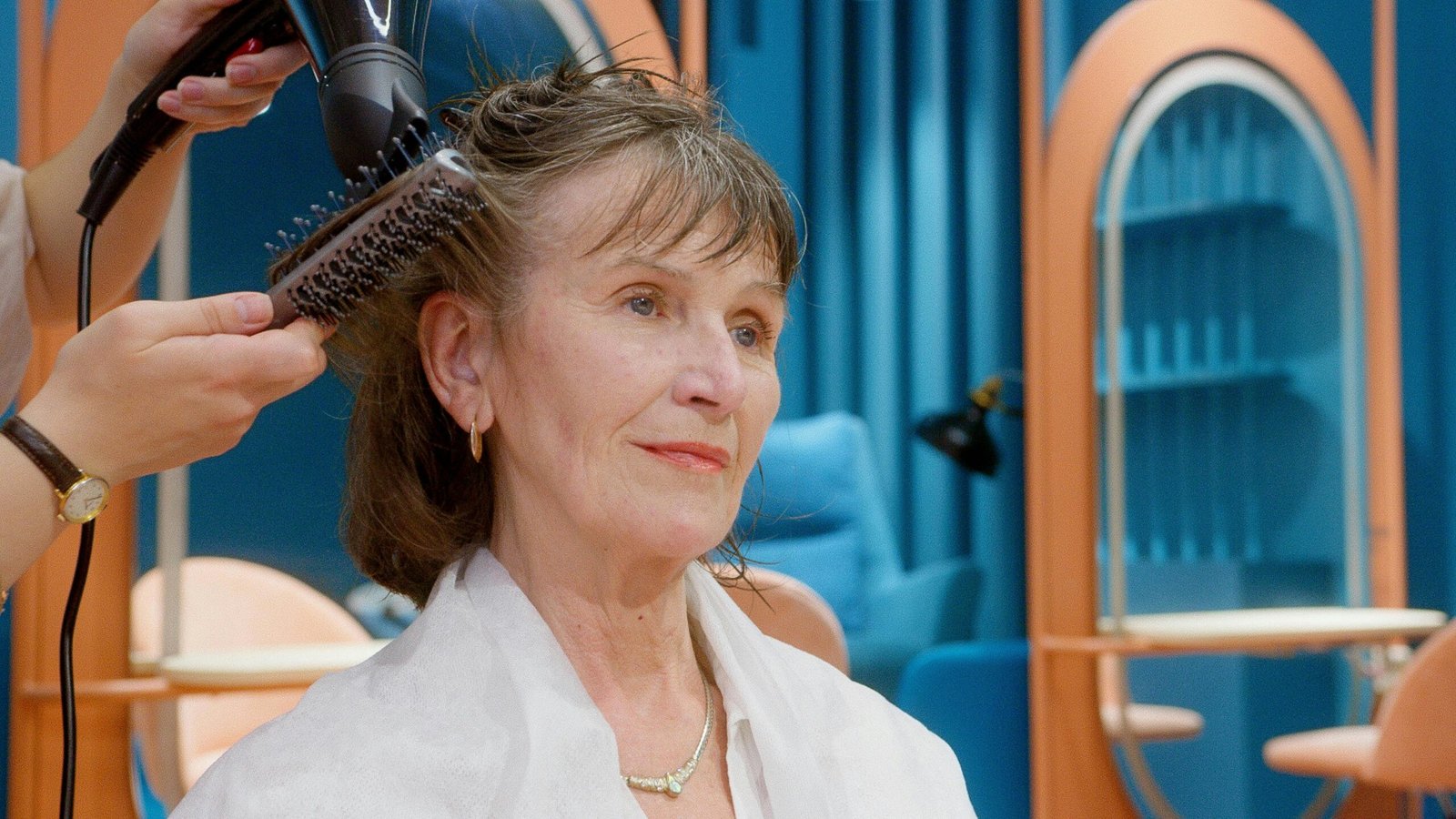 A senior woman receives hairstyling and pampering in a modern salon setting.